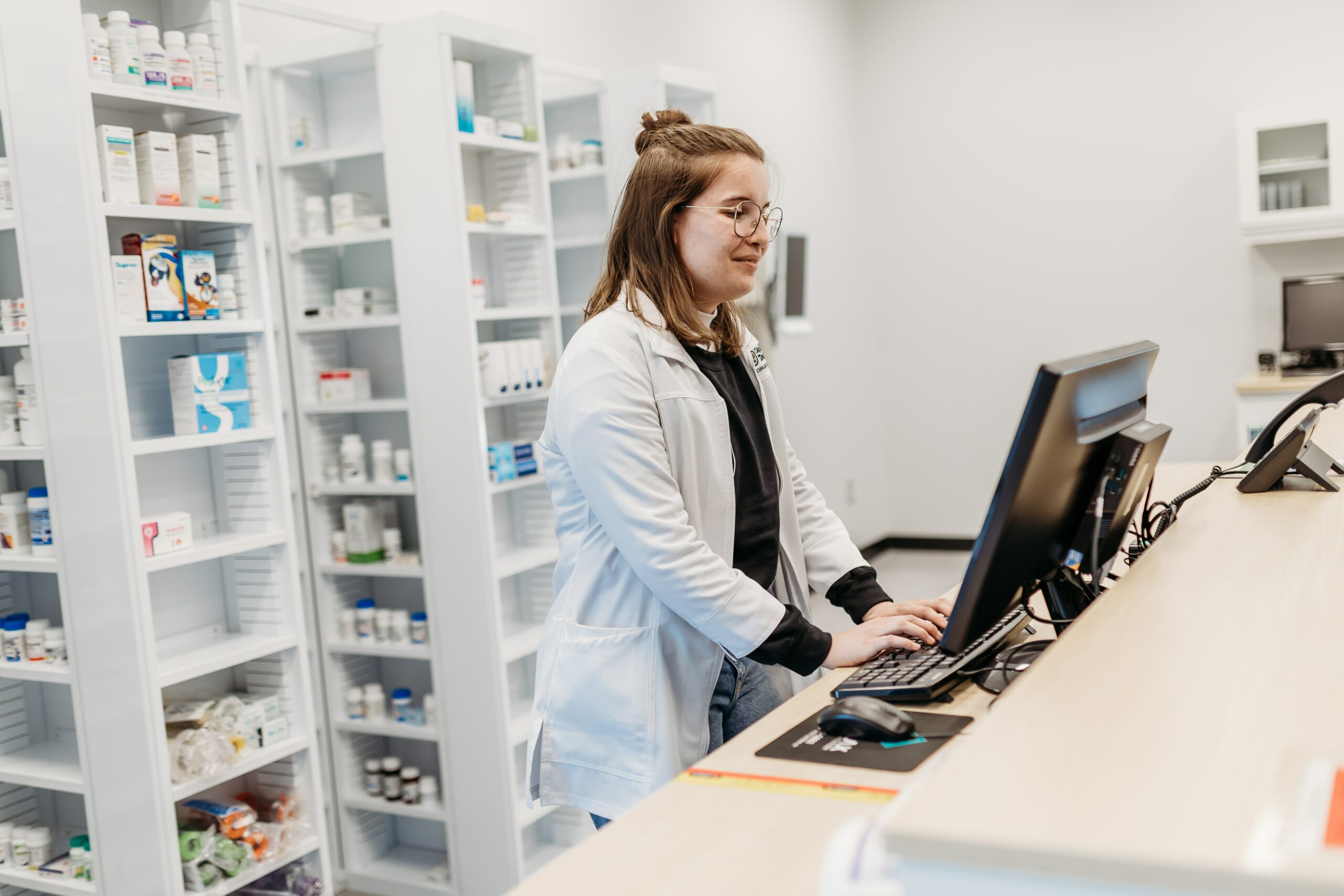 Une jeune femme travaille sur son ordinateur dans un environnement de pharmacie.