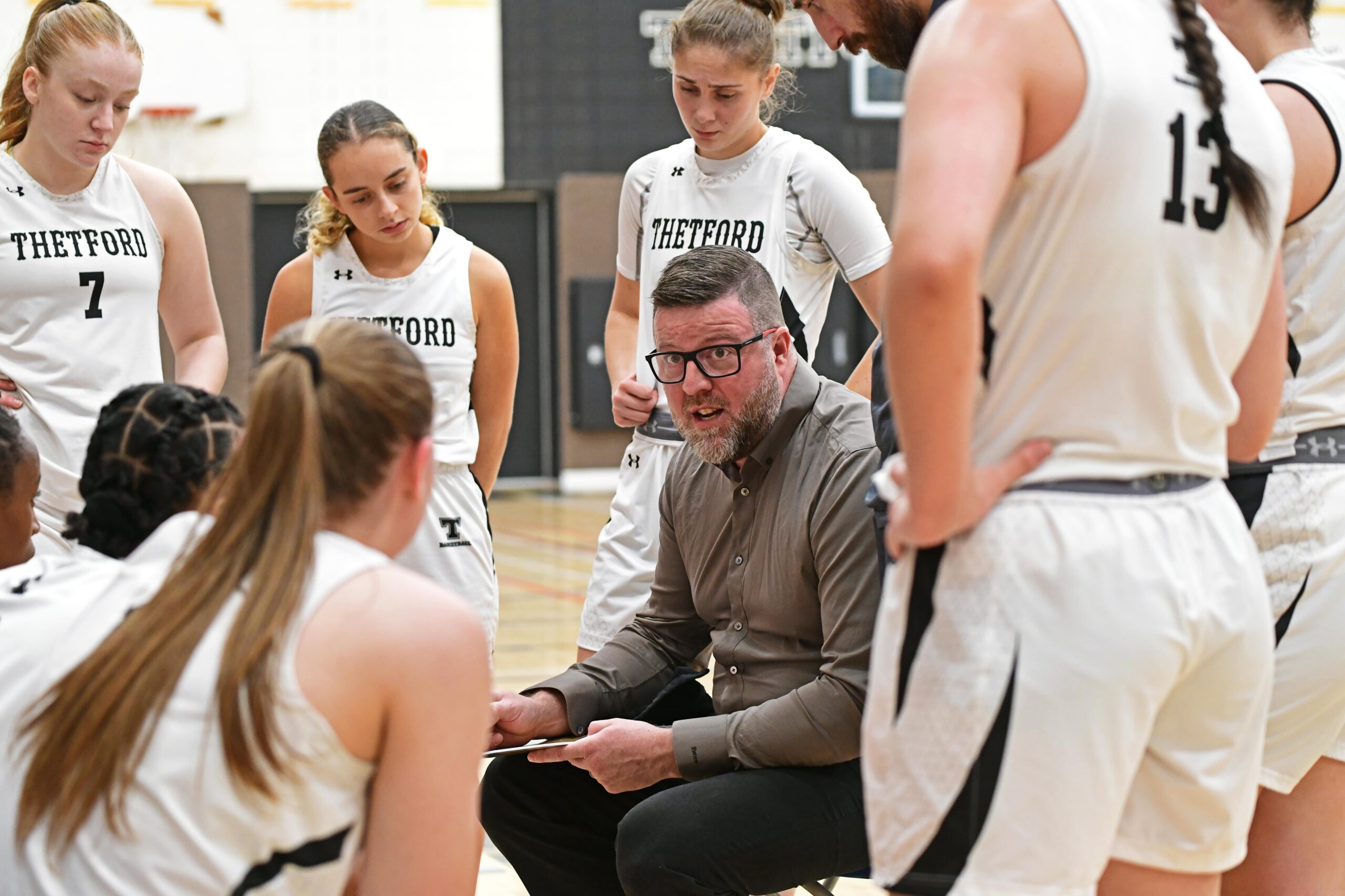 Caucus stratégique lors d'une partie de basketball collégial féminin de l'équipe du Cégep de Thetford. L'entraîneur s'adresse aux joueuses lors d'un temps d'arrêt.
